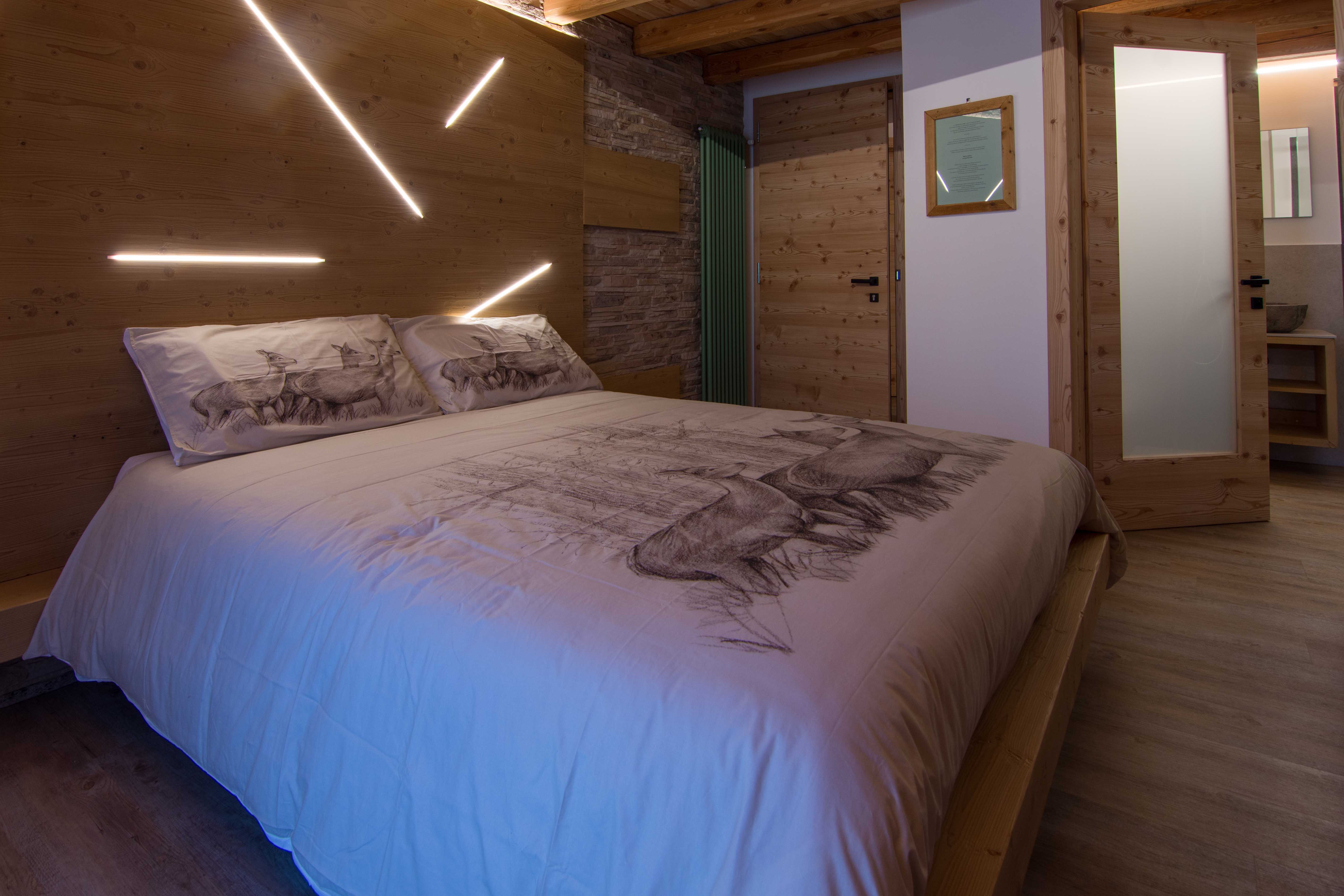 Camera Prieda. Dormire in camera spaziosa e romantica. Decorazioni raffinate in legno con paesaggi di montagna tipici della Val di Non.