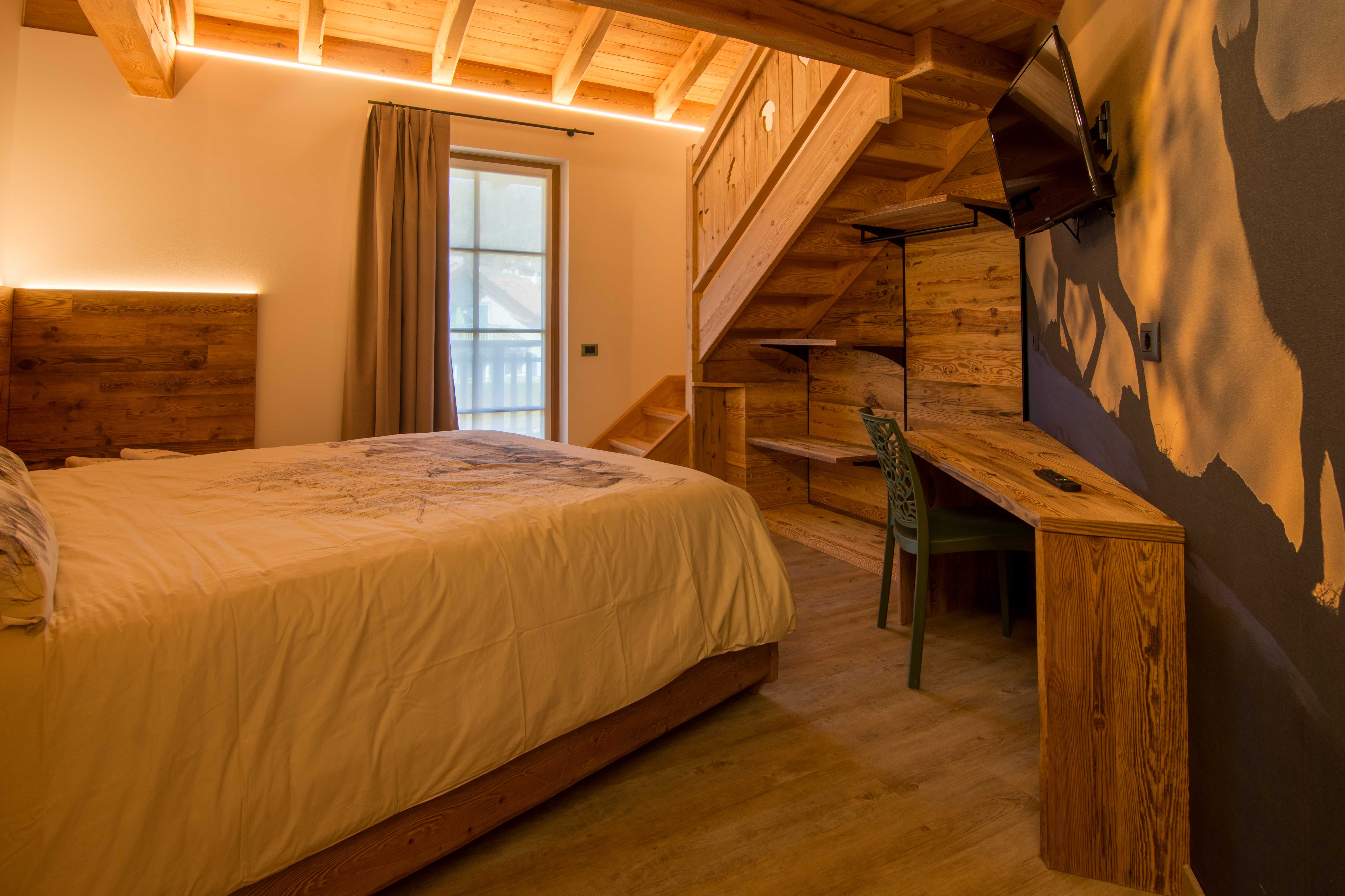 Camera Sorasu. Camera spaziosa con scrivania e decorazioni raffinate in legno con paesaggi di montagna tipici del Trentino.