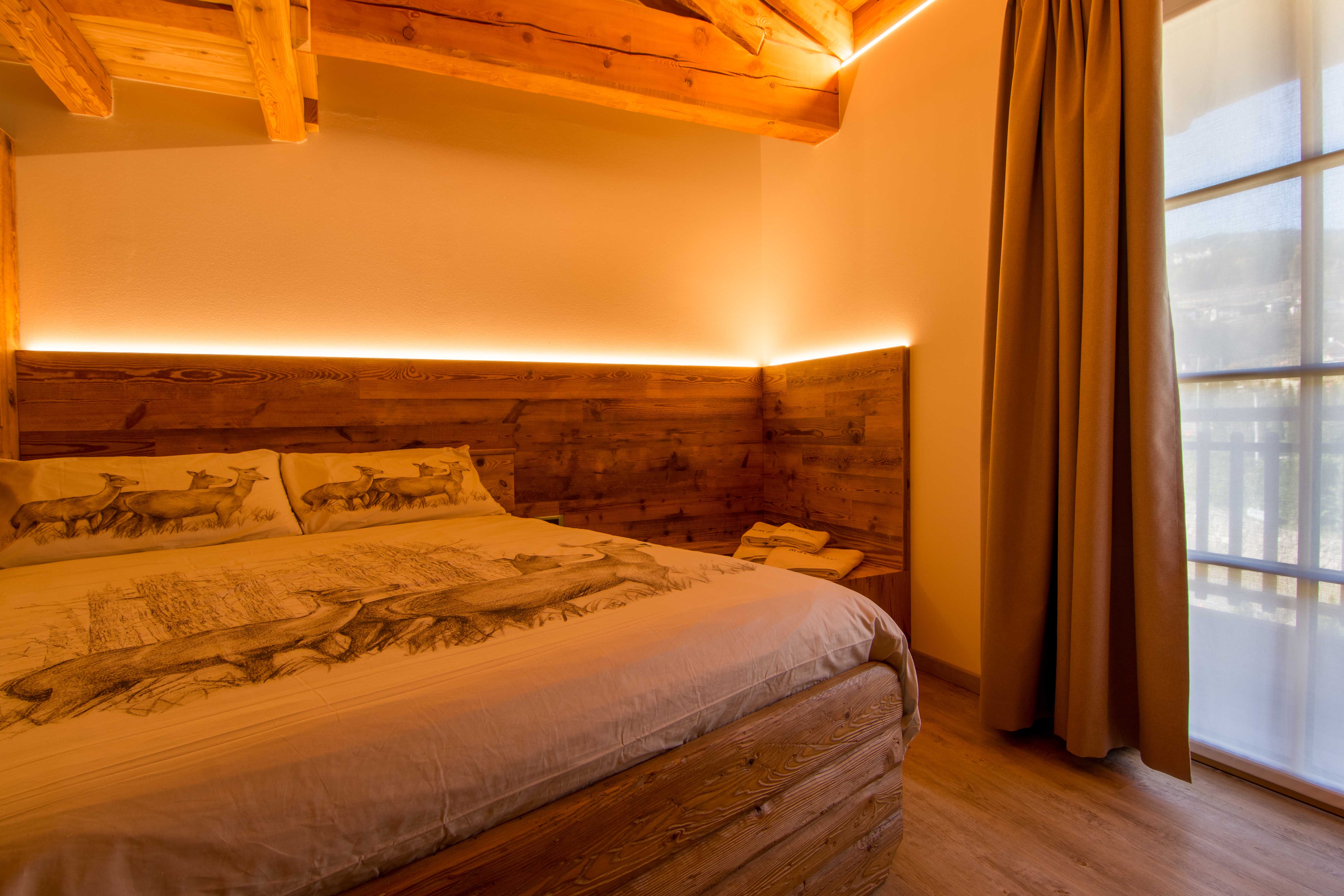 Camera Sorasu. Dormire in camera spaziosa e romantica. Decorazioni raffinate in legno con paesaggi di montagna tipici della Val di Non.